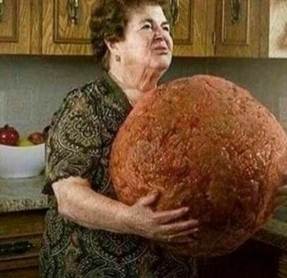 Older woman standing in kitchen, holding a gigantic meatball.