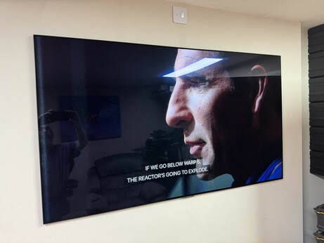 An image of a television displaying a close-up of a man's face with a tense expression, accompanied by text that reads, "IF WE GO BELOW WARP 5, THE REACTOR'S GOING TO EXPLODE."