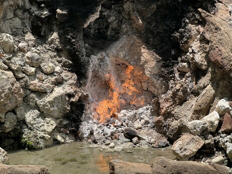 A stone alcove containing a bubbling spring with an open fire burning on top of it.
