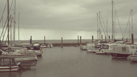 Photo of a small yacht pier at the german north sea coast. There are a few boats with the sea in the background.