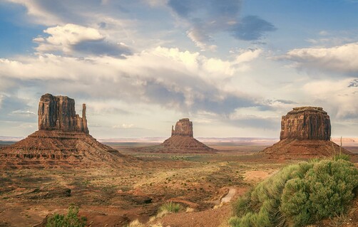 Three large rock formations, West Mitten, East Mitten, and Merrick Butte, in Monument Valley Arizona under a dramatic cloudy sky.
