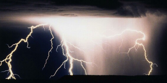 A thunderstorm at night - lightning bolts illuminate falling rain and clouds, and the dark horizon can be seen at the bottom of the frame.