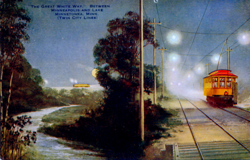 Night time view of a trolley on the right heading down the tracks. There are bright white lights guiding the way. On the left is a river and trees and a trolley at the far end of the river.